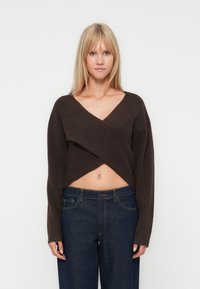 Pull court marron avec un décolleté en V profond et des manches amples, fabriqué à partir d'un matériau tricoté doux ; associé à un jean large bleu foncé.