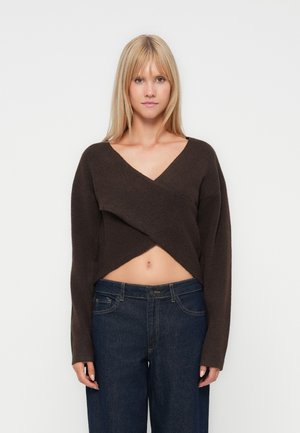 Bruine cropped trui met een diepe V-hals en losse mouwen, gemaakt van een zachte breimateriaal; gecombineerd met donkerblauwe wijde jeans.