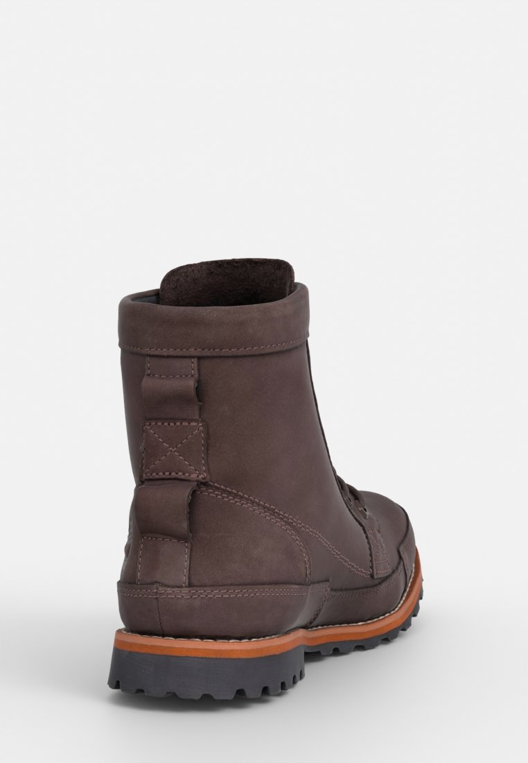 Botín de cuero marrón, con punta redondeada, cuello acolchado y suela de goma texturizada. Presenta costuras visibles y un acabado mate.