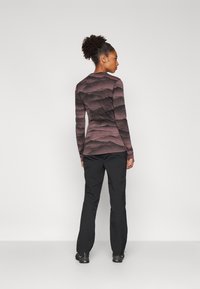 Langermige top in gemusterde tinten van bordeauxrood en zwart met een getailleerd ontwerp, gecombineerd met zwarte broek en donkere schoenen.