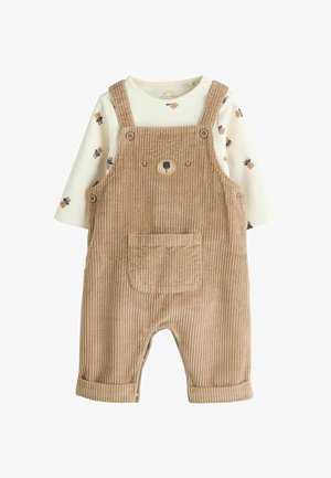 Teddybruine corduroy salopette met schouderbanden, voorzien van een berengezichtontwerp en een voorkruiszak. Onder de salopette ligt een wit longsleeve shirt met berenprints.