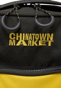 Sort og gul stofpose med "CHINATOWN MARKET" broderet i gult, med gummibelagt hardware og kontraststing.