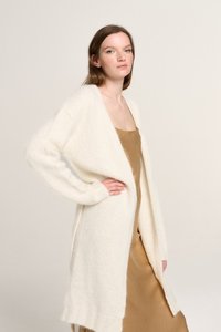 Langer cardigan mit offener Vorderseite aus weichem cremefarbenem Strick, mit weiten Ärmeln und gerippten Bündchen, über einem glatten, beigen Unterkleid. 
