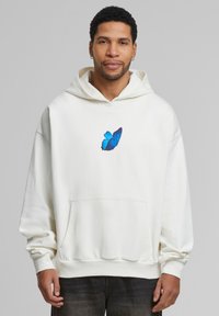 Hvid hoodie lavet af blødt stof, med et blåt sommerfuglegraphic på brystet, kængurulomme og ribkant på ærmer og kant.