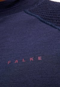 Marineblaues sportliches Oberteil aus strukturiertem Stoff mit glatten Abschnitten. Verfügt über einen gerippten Kragen und die Marke "FALKE" in Dunkelrot gedruckt.