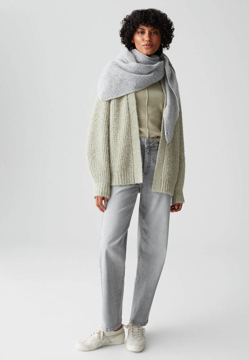 Cardigan texturé vert clair sur un haut gris clair, associé à un jean gris taille haute et des baskets blanches. Écharpe grise drapée avec style.