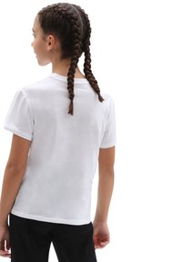 Camiseta blanca de algodón con mangas cortas, escote redondo y una textura suave, utilizada por una persona con dos trenzas, de espaldas a la cámara.