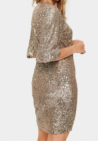 Gul paljetterad klänning med en figurnära siluett, trekvartsärmar och knälång nederkant. Texturen är glänsande och reflexiv.