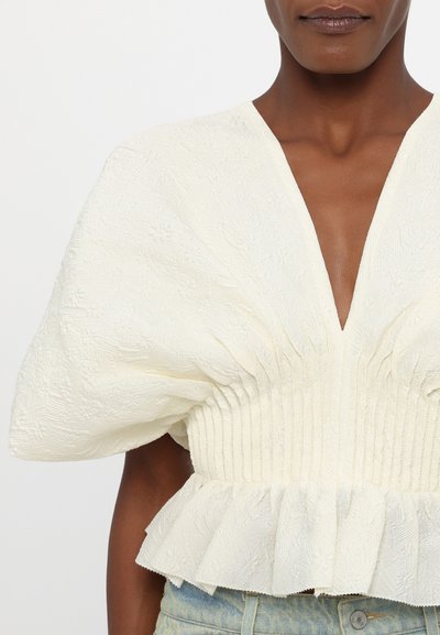 Elfenben peplum bluse med voluminøse pufærmer, tekstureret blomstermønster, dyb V-udskæring og smocked taljedetalje.
