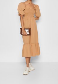 Beige midiklänning med puffärmar, smockad byst och lagererad nederkant. Matchad med en blank brun clutch och krämfärgade snörskor.