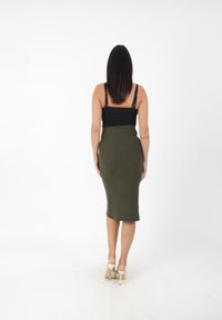 Top nero senza maniche e gonna midi verde oliva, taglio aderente, texture liscia e una leggera lucentezza; persona che indossa scarpe con tacco trasparenti, vista da dietro.