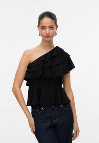 Haut noir à une épaule avec des volants superposés, taille élastique et silhouette en peplum, associé à un jean bleu foncé. Texture de tissu lisse.