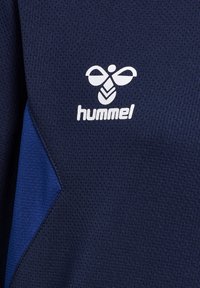 Marineblaue Sporttrikot aus strukturiertem Stoff, mit blauen Panelakzenten und einem weißen "hummel"-Logo mit einem Bienenmuster auf der Brust.
