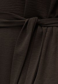 Κοντινή λήψη σκούρου καφέ υφάσματος δεμένου σε κόμπο, με έμφαση στην υφή και τις λεπτομέρειες της πτώσης.