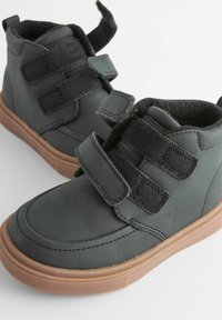 Graue High-Top-Schuhe aus glattem synthetischem Material mit zwei verstellbaren schwarzen Klettverschlüssen und einer braunen Gummisohle.