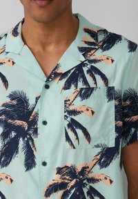 Kortekoo shirt van lichte teal stof, met een marineblauw palmbladpatroon en perzikkleurige accenten. Inclusief een borstzak en zwarte knopen.