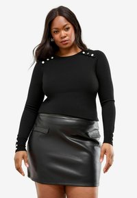 Zwarte lange mouwen top met knoopdetails op de schouders, gecombineerd met een zwarte leren minirok met twee voorzakken.