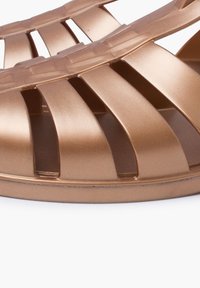 Bronze, textured plastic slide sandal features horizontal cutouts and a contoured sole, designed for breathability and comfort.