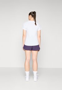 Hvid kortærmet T-shirt med rund hals, parret med lilla træningsshorts, der har en afslappet pasform og en glat stoftekstur.