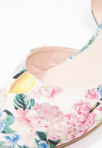 Chaussure à enfiler fleurie avec une tige en toile ornée de fleurs roses, bleues et jaunes ; doublure intérieure lisse beige ; design à bout pointu.