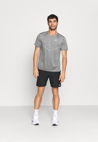Camiseta Nike gris de manga corta con pantalones cortos deportivos negros. La camiseta presenta un sutil patrón texturizado y un detalle del logo en el pecho.