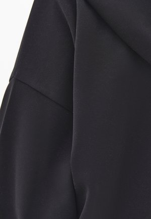 Close-up van glad zwart stof met zichtbare naad en gevouwen lagen, die de textuur en val laten zien.