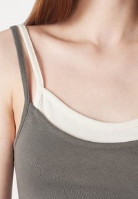 Dwuwarstwowe topy: szary zewnętrzny z cienkimi ramiączkami i kremowy wewnętrzny. Oba wykonane z miękkiej, elastycznej tkaniny.