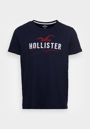 Marineblaues T-Shirt mit kurzen Ärmeln mit weißem „HOLLISTER“-Schriftzug, rotem Möwenlogo darüber und rotem kursivem „California“ unter dem Schriftzug.