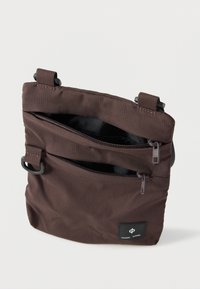 Hnedá textilná taška s textúrovaným povrchom, s dvoma vreckami na zips a nastaviteľnými popruhmi. Na prednej strane sa nachádza čierna logo nálepka.