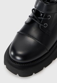 Black leather ankle boot with a rounded toe, sturdy sole, and lace-up design. Features stitching accents and metallic eyelets for laces.