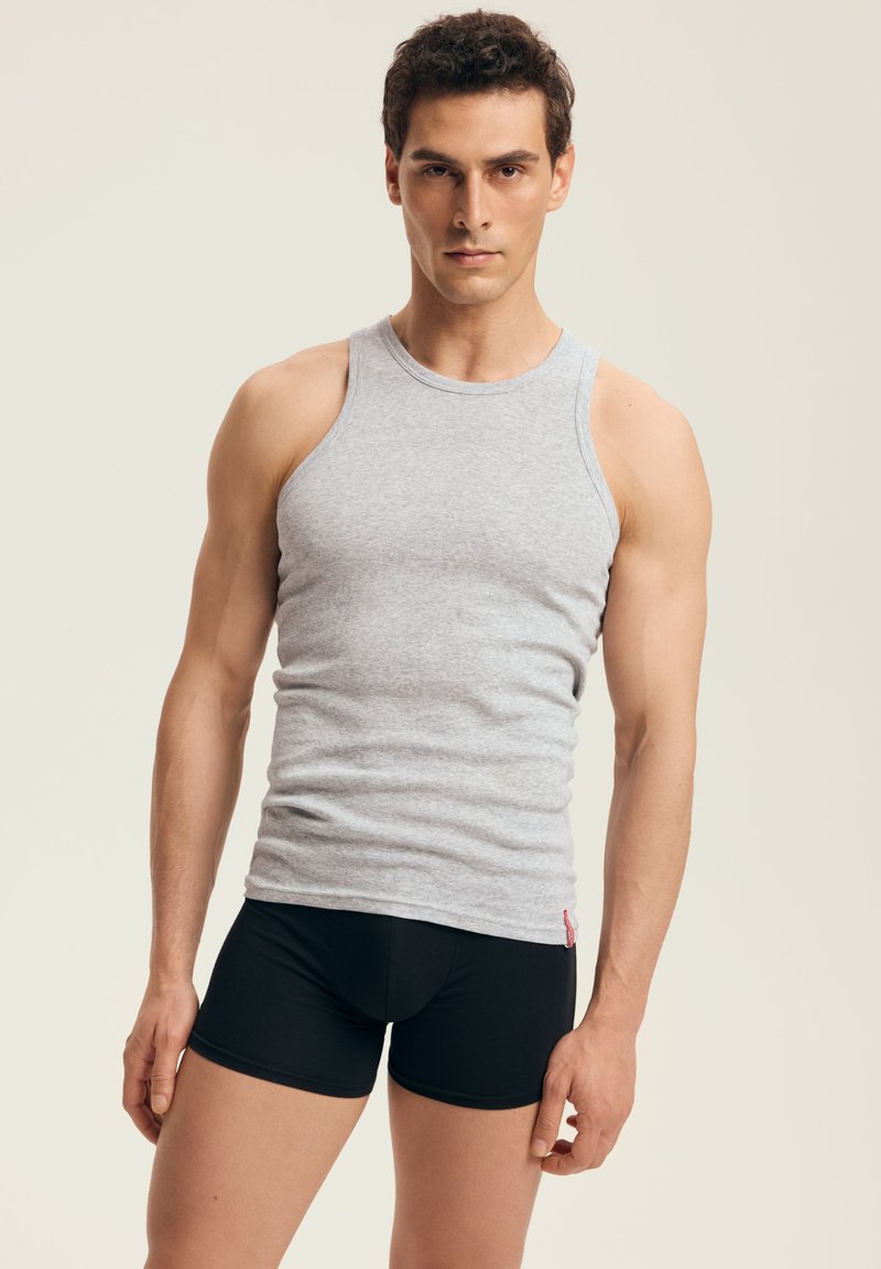 Szary top bez rękawów z okrągłym dekoltem, wykonany z miękkiego materiału. Noszony z czarnymi dopasowanymi szortami, podkreślającymi wzór i teksturę obu ubrań.