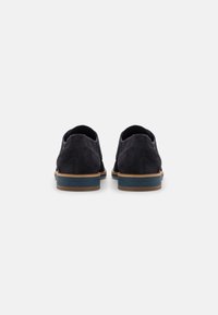 Dunkelmarineblaue Wildlederschuhe mit einer strukturierten Rückseite, einer kontrastierenden hellen Sohle und einem schmalen marineblauen Akzent entlang der Ferse. Klassisches Design.