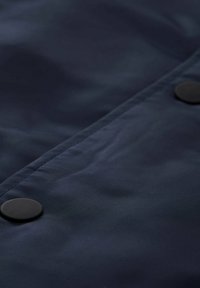 Tejido azul marino con una textura suave y dos botones a presión negros a lo largo de la costura, destacando un diseño minimalista y funcional.