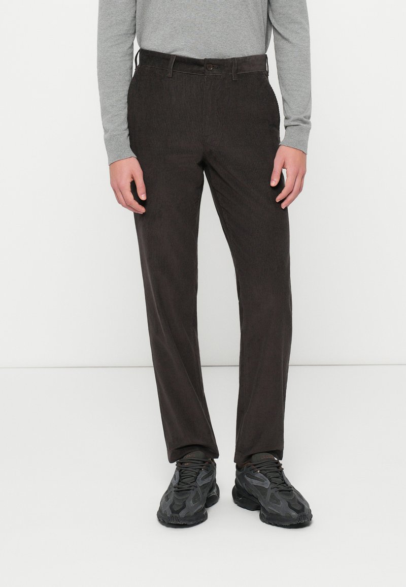 Pantalons en velours côtelé marron à coupe droite, dotés d'une fermeture à bouton et de poches latérales, accompagnés d'une chemise �à manches longues grise et de baskets noires.