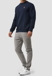 Marineblauwe trui met honingraatstructuur, ronde hals en geribbelde manchetten, gecombineerd met lichtgrijze slim-fit broek en witte sneakers.