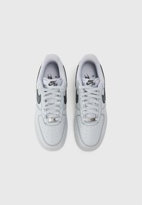 Nike Air Force 1 kedas balta āda ar melniem akcentiem. Iespējas ietver perforētu pirksta daļu, plakanu šņoru un metālisku sudraba birku.