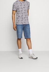 Grå t-shirt med svart palmträdsmönster, ihopparad med jeansshorts. Bärs med vita strumpor och grå sportskor. Ren design, avslappnad stil.