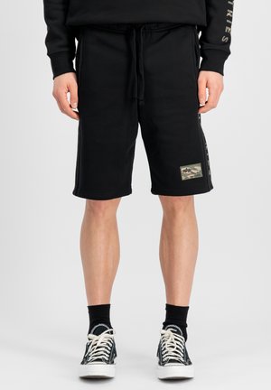 Black cotton shorts with an elastic waistband and drawstring, featuring a camouflage patch on the left leg and side logo detailing.