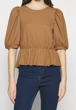 Top marrone con texture, scollatura rotonda, maniche a sbuffo e vita stretta che porta a un orlo svasato. Abbinato a jeans blu scuro.