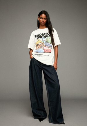 Oversized cream t-shirt with "Radiator Springs" graphic and blue denim wide-leg pants. Smooth texture, casual design, with a relaxed fit.