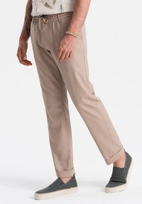 Pantaloni beige con cordoncino, dal taglio affusolato e orli a risvolto, abbinati a scarpe slip-on grigie con una tomaia testurizzata e suola a contrasto.