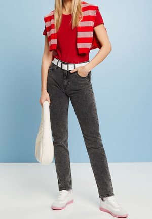 Červené tričko s krátkým rukávem, šedé džíny s vysokým pasem, bílý opasek, bílá taška a bílé tenisky s růžovými akcenty. Pruhovaná mikina přehnutá přes ramena.