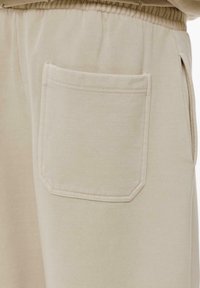 Beige Sweatpants mit einer rechteckigen Gesäßtasche, klassischer Naht und weichem, strukturiertem Stoff. Elastischer Bund.