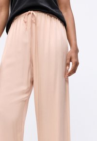 Lichtroze wijde broek met een gladde stofstructuur, voorzien van een elastische tailleband en een trekkoorddetail aan de voorkant.