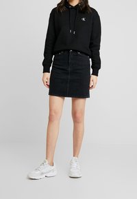 Haut à capuche noir avec logo, associé à une mini jupe en denim et des baskets blanches. La jupe présente une coupe droite, une couture sur le devant et un minimum de détails.