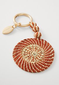 Porte-clés rond tissé composé de matériaux rouges et crème. Dispose d'un anneau en métal doré et de perles tissées décoratives.