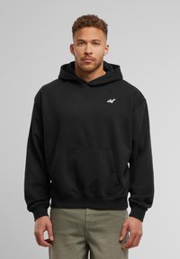 Sweatshirt à capuche noire en coton, avec une poche frontale et un logo brodé en blanc. Coupe ample, avec des poignets côtelés.