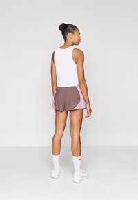 Camiseta blanca sin mangas con textura acanalada combinada con pantalones cortos para correr en marrón y lila, con un diseño ligero, ajuste atlético y detalles de costuras visibles.