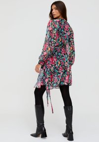 Florales Kleid mit langen Ärmeln, mehrfarbiges Muster auf transparentem Stoff, tailliert, mit Rüschensaum, kombiniert mit schwarzen kniehohen Stiefeln.