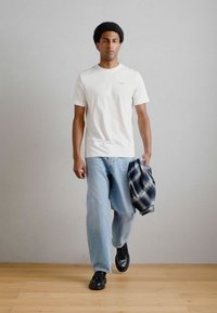 Balta īsām piedurknēm t-kreklu, gaiši zilo brīvi pieguļošo džinsu un melnas kurpes. Uz kreisā roka ir uzlikta flaneļa krekla.